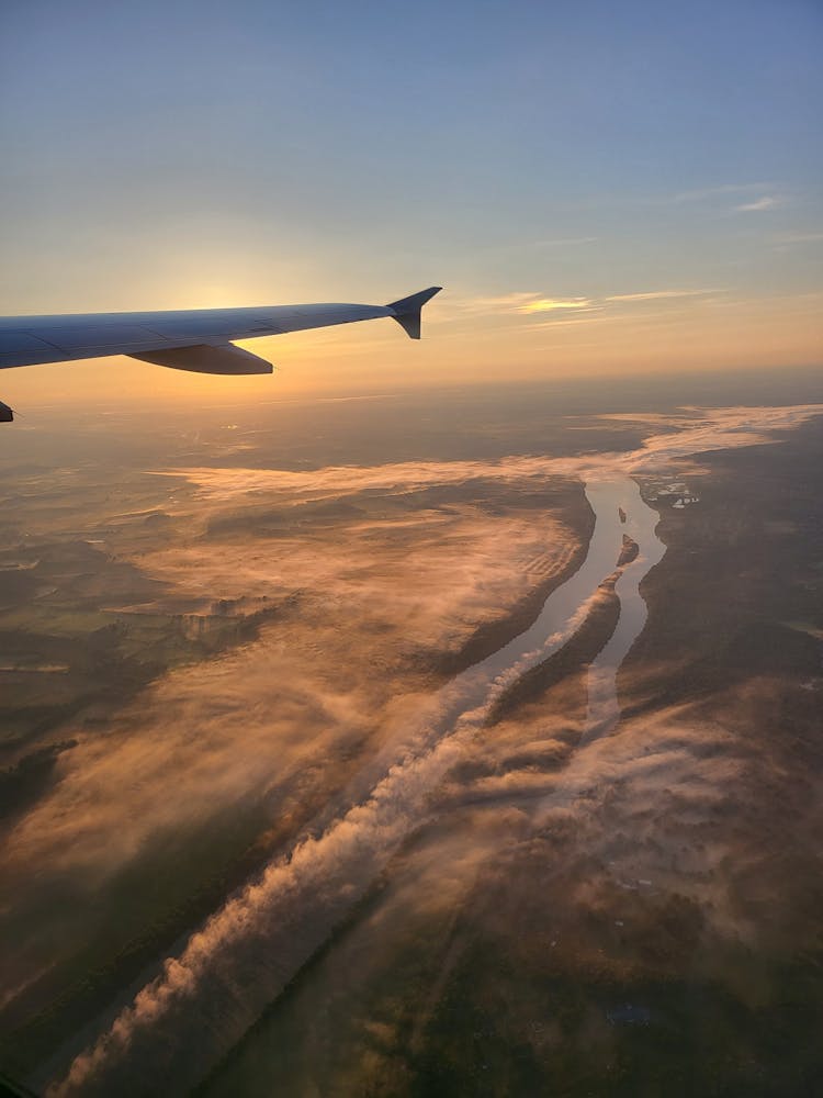 River And Plains Below Airplane Wing At Sunset