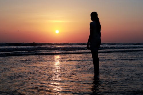 Silhouette of Woman Standing on Sea Shore at Sunset