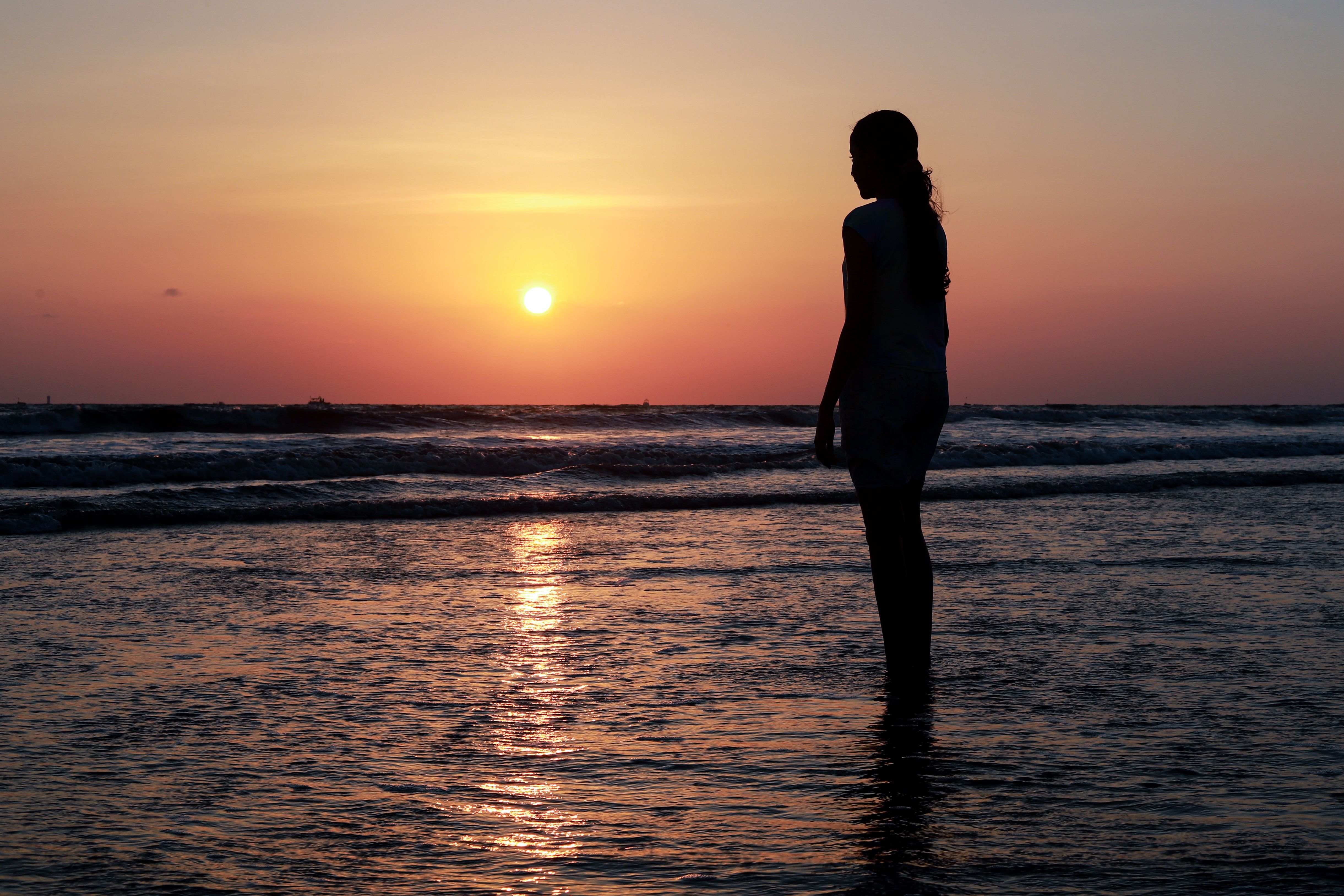 Silhouette of Woman Standing on Sea Shore at Sunset · Free Stock Photo