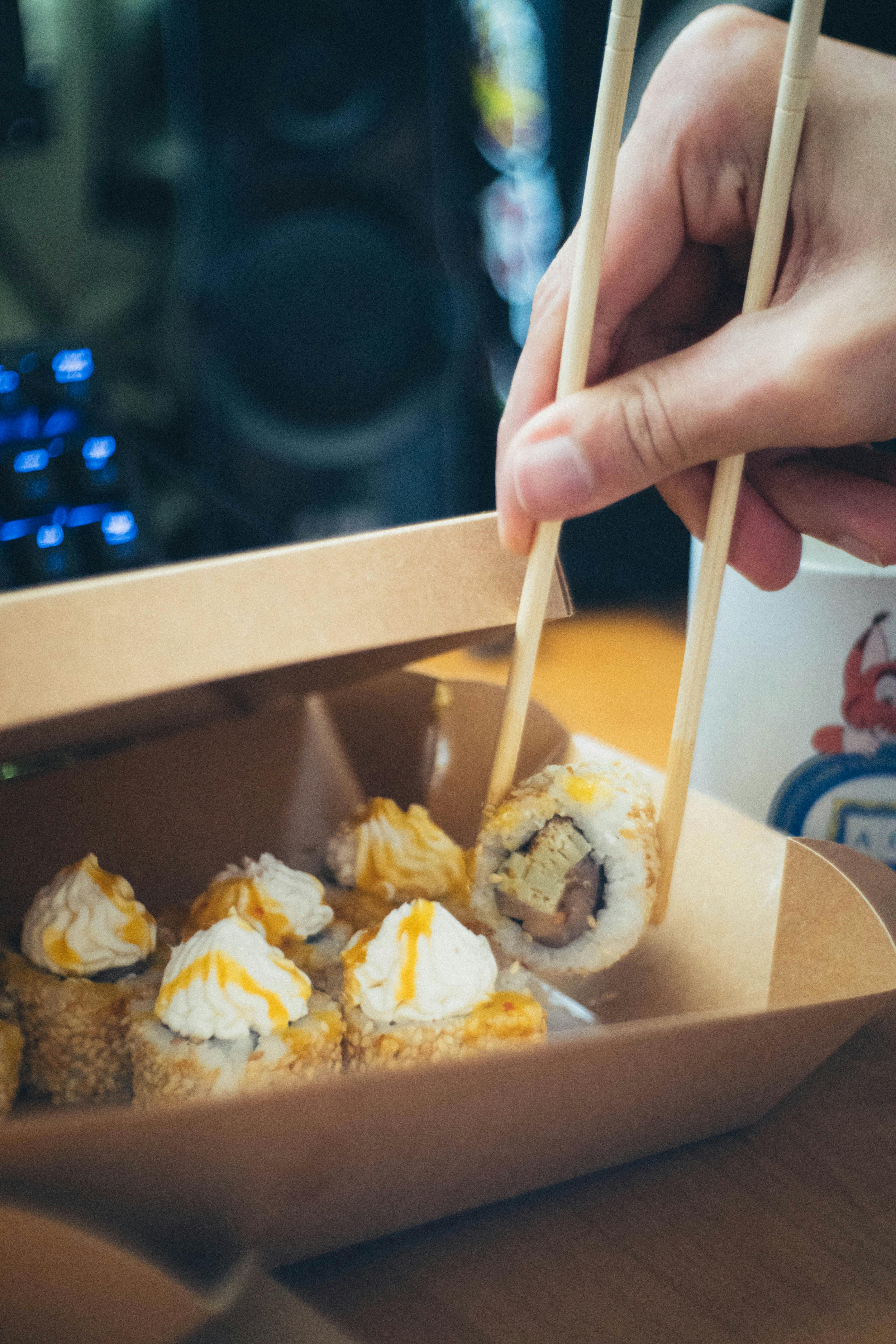 a person holding chopsticks over sushi in a box