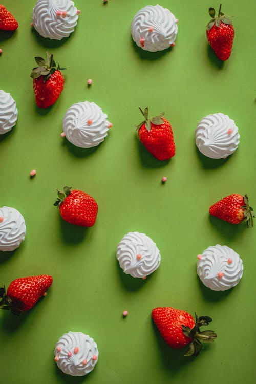 Strawberries and Meringue with Sprinkles Lying on Green Background