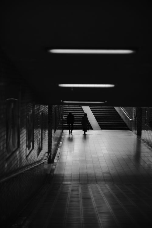 Free Two people walking in a dimly lit underground tunnel towards stairs. Stock Photo