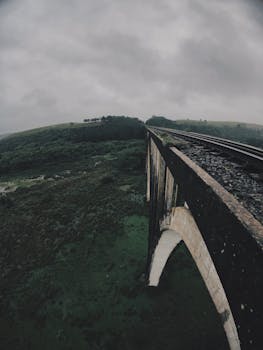 鸟瞰图中，一座铁路桥横跨郁郁葱葱的绿色山谷，天空多云