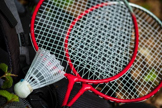 Two red badminton rackets and a shuttlecock on a backpack outdoors, perfect for leisure and sports activities.