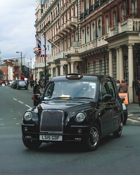Black taxi driving through London's bustling streets, showcasing iconic urban architecture.