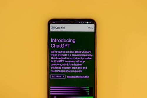 Free Mobile phone displaying the ChatGPT introduction screen with OpenAI branding on a yellow background. Stock Photo