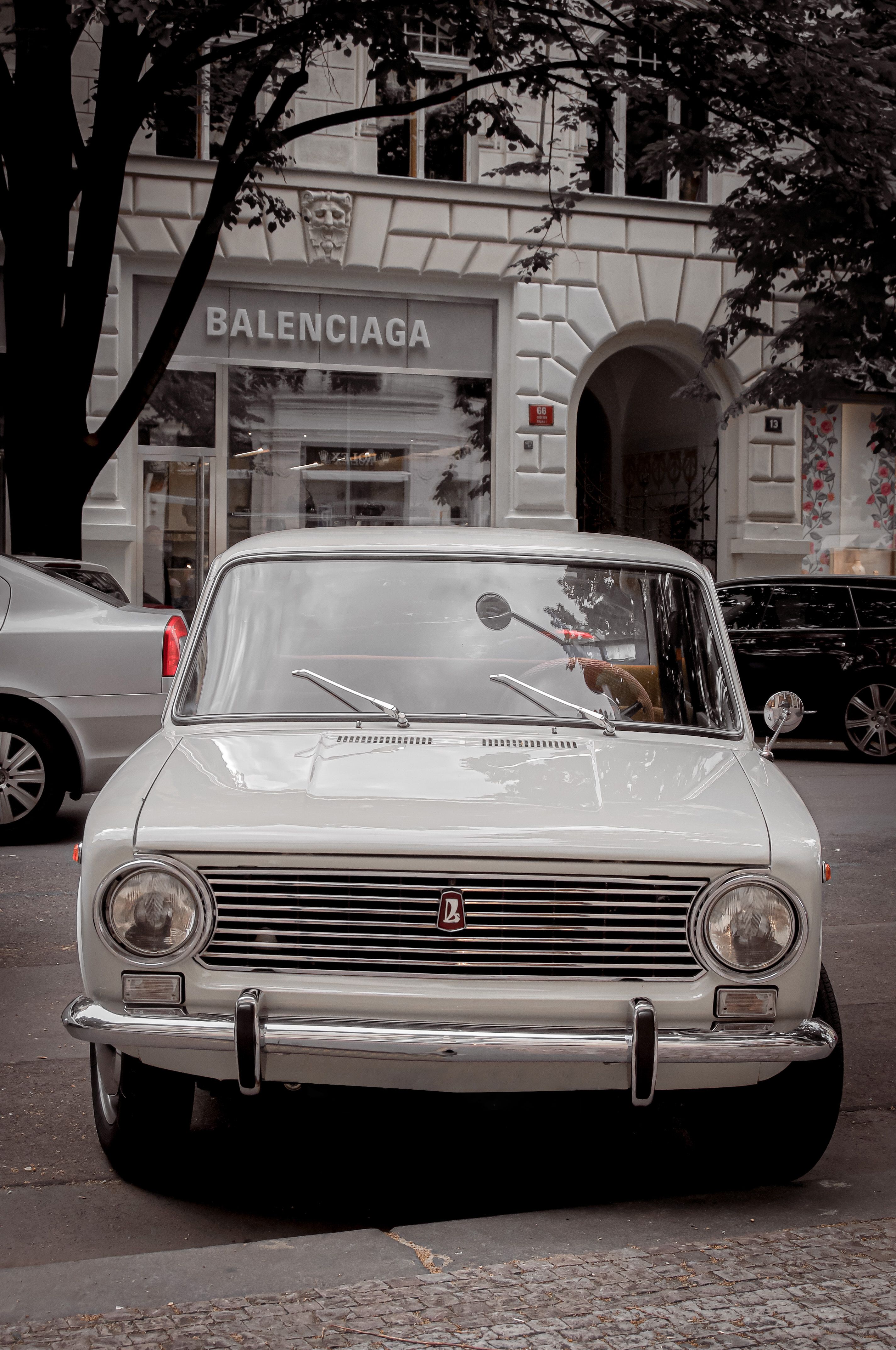 A retro VAZ-2101 car parked on a street in Prague, contrasting with a Balenciaga storefront.