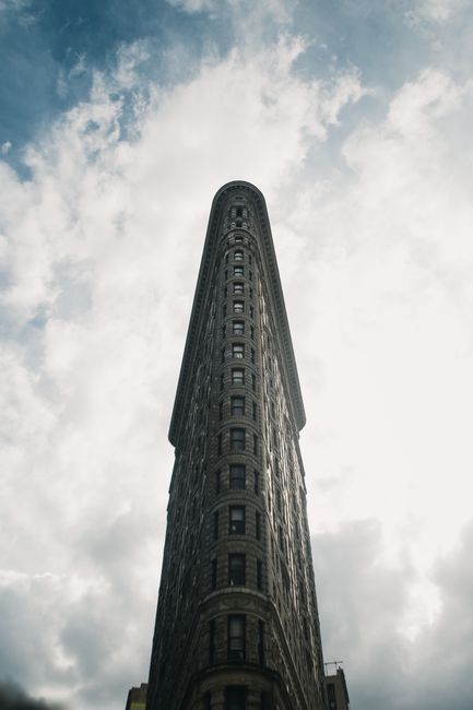 Vertical shot of the iconic Flatiron Building in New York City against a dramatic cloudy sky.