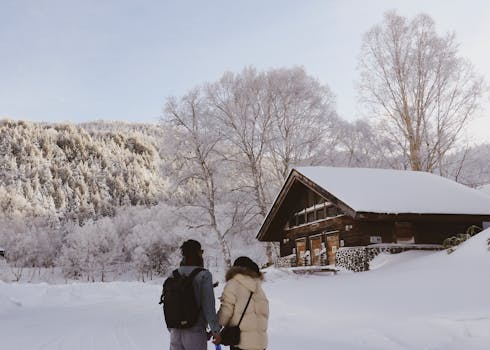 一对夫妇走过白雪皑皑的冬季风景，背景是一间小屋