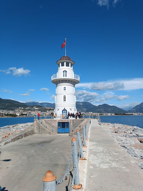 Free A scenic view of Alanya Lighthouse on a sunny day with a clear blue sky and mountain background. Stock Photo