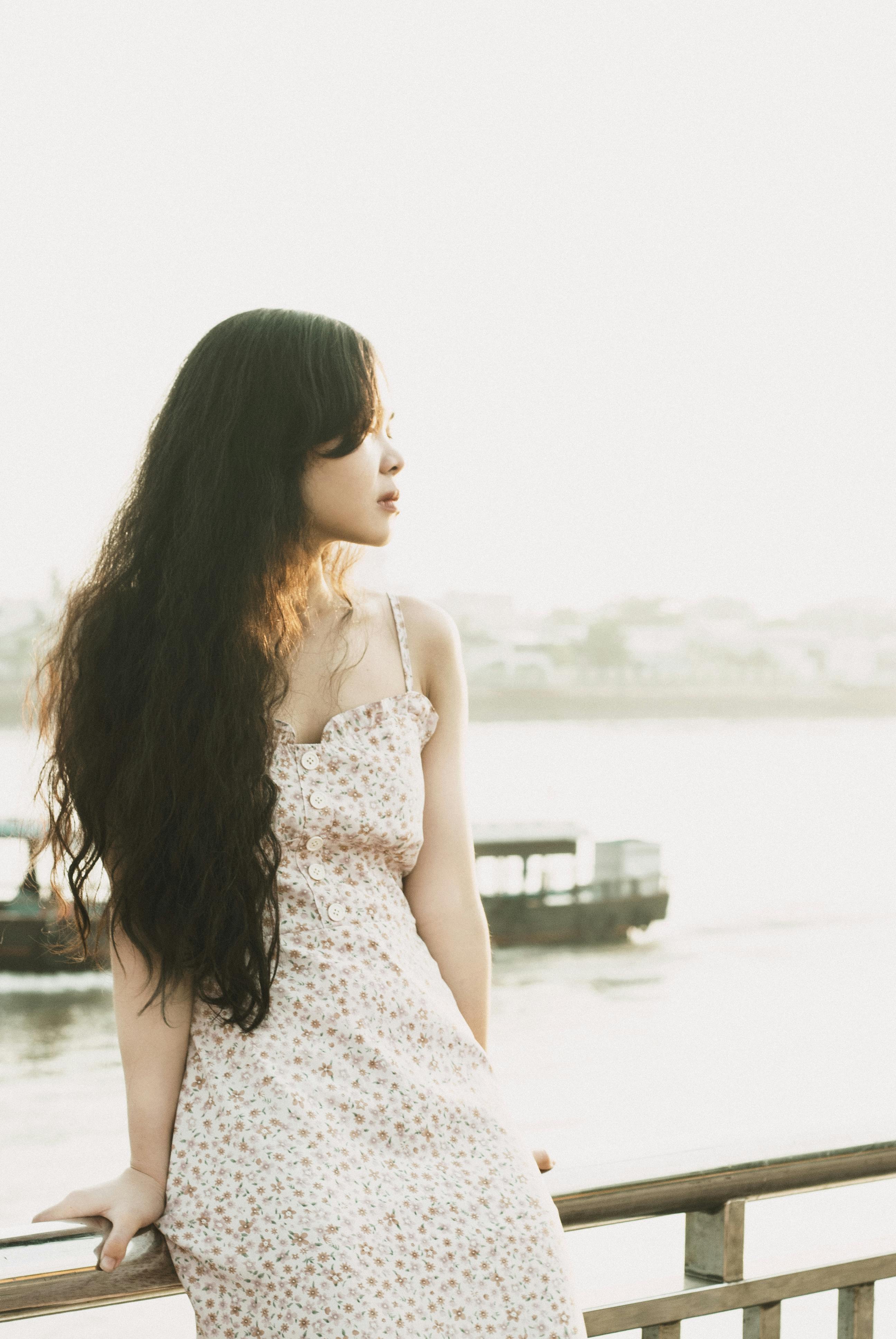 Portrait of a young woman sitting by the river in a summer dress, looking relaxed.