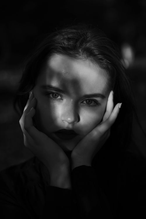 Free Striking black and white portrait of a woman with hands on her face, dramatic lighting. Stock Photo