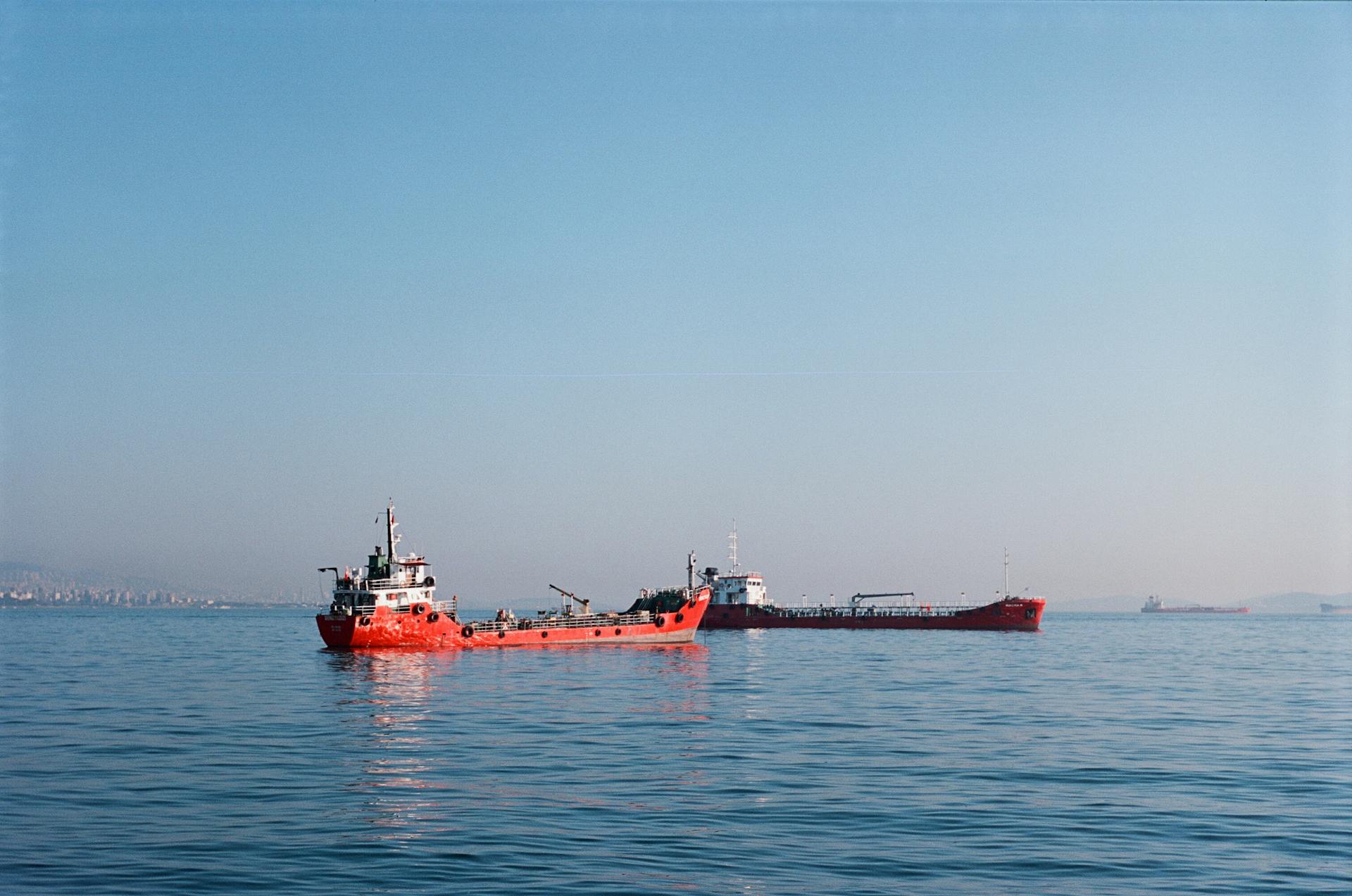 Red cargo ship on tranquil blue sea with distant land visible, ideal for logistics theme.