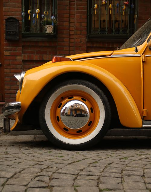 Free A close-up of a vintage yellow car's wheel on a cobblestone street with decorative brick background. Stock Photo