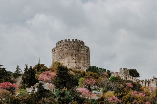 Free A stunning view of the Rumelian Fortress in Istanbul, surrounded by vibrant spring foliage under a cloudy sky. Stock Photo