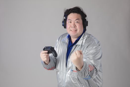 Asian man with headphones celebrates while gaming, holding a controller.