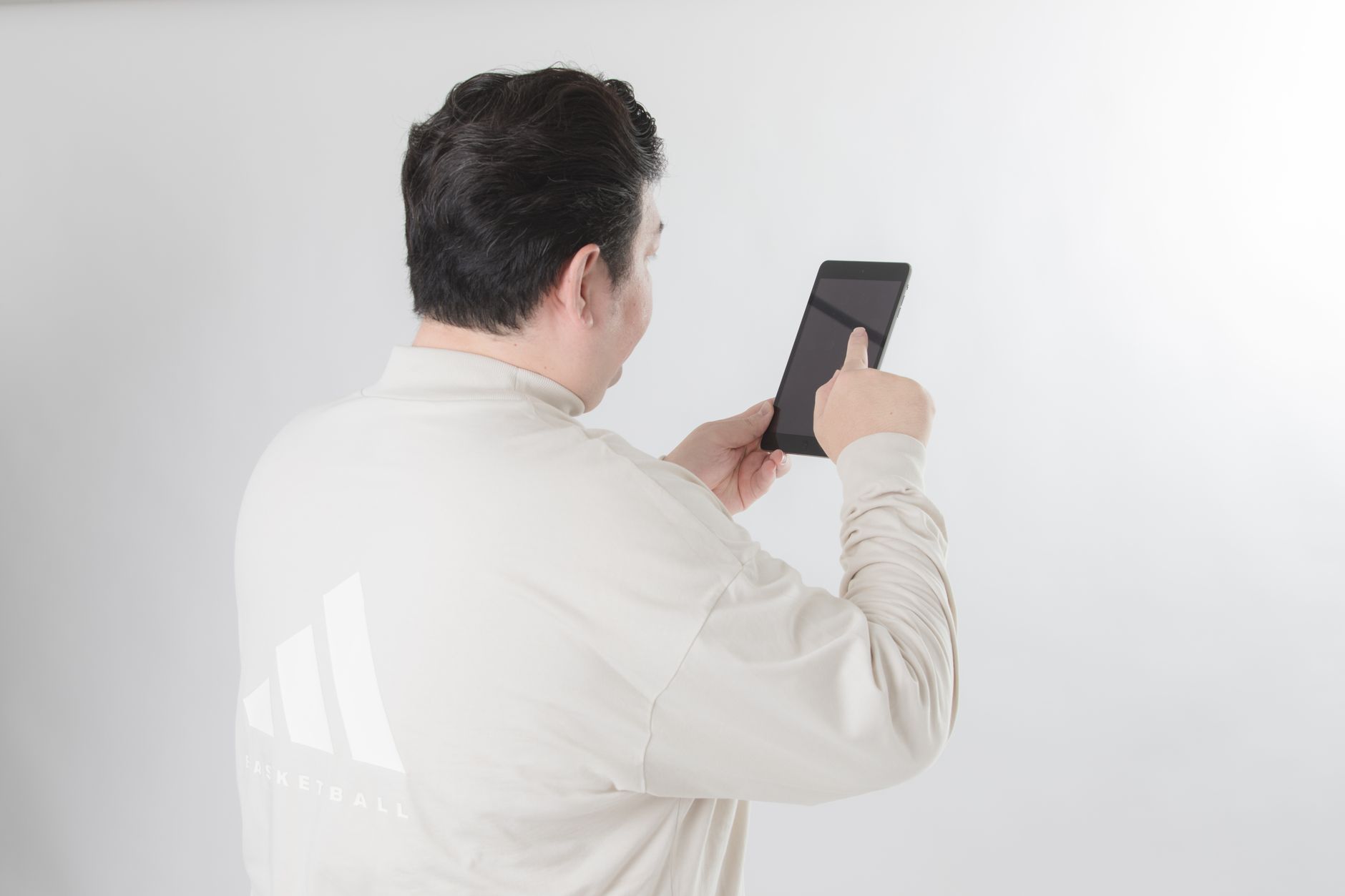 Man with black hair using a tablet on a white background, focusing on the screen.