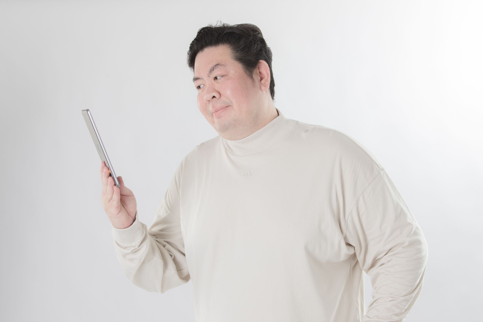 Portrait of an adult man holding a tablet device, gazing thoughtfully against a white backdrop.