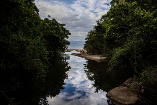 Picturesque river and lush greenery in Angra dos Reis, Brazil, reflecting a cloudy sky.