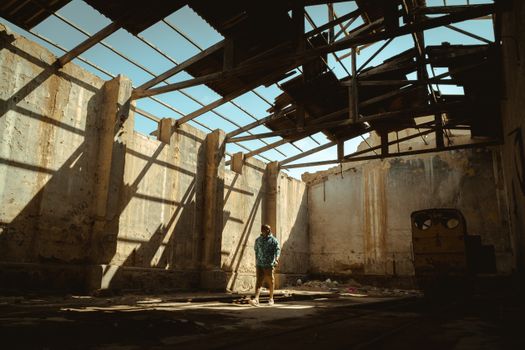 Man standing in a sunlit, abandoned warehouse in Chicama, capturing an urban decay scene.