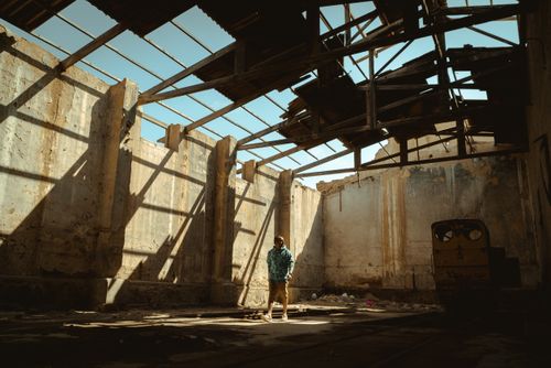 Free Man standing in a sunlit, abandoned warehouse in Chicama, capturing an urban decay scene. Stock Photo