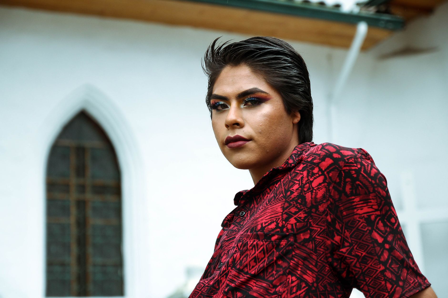Elegant portrait of a young model in a red patterned shirt posing outdoors.