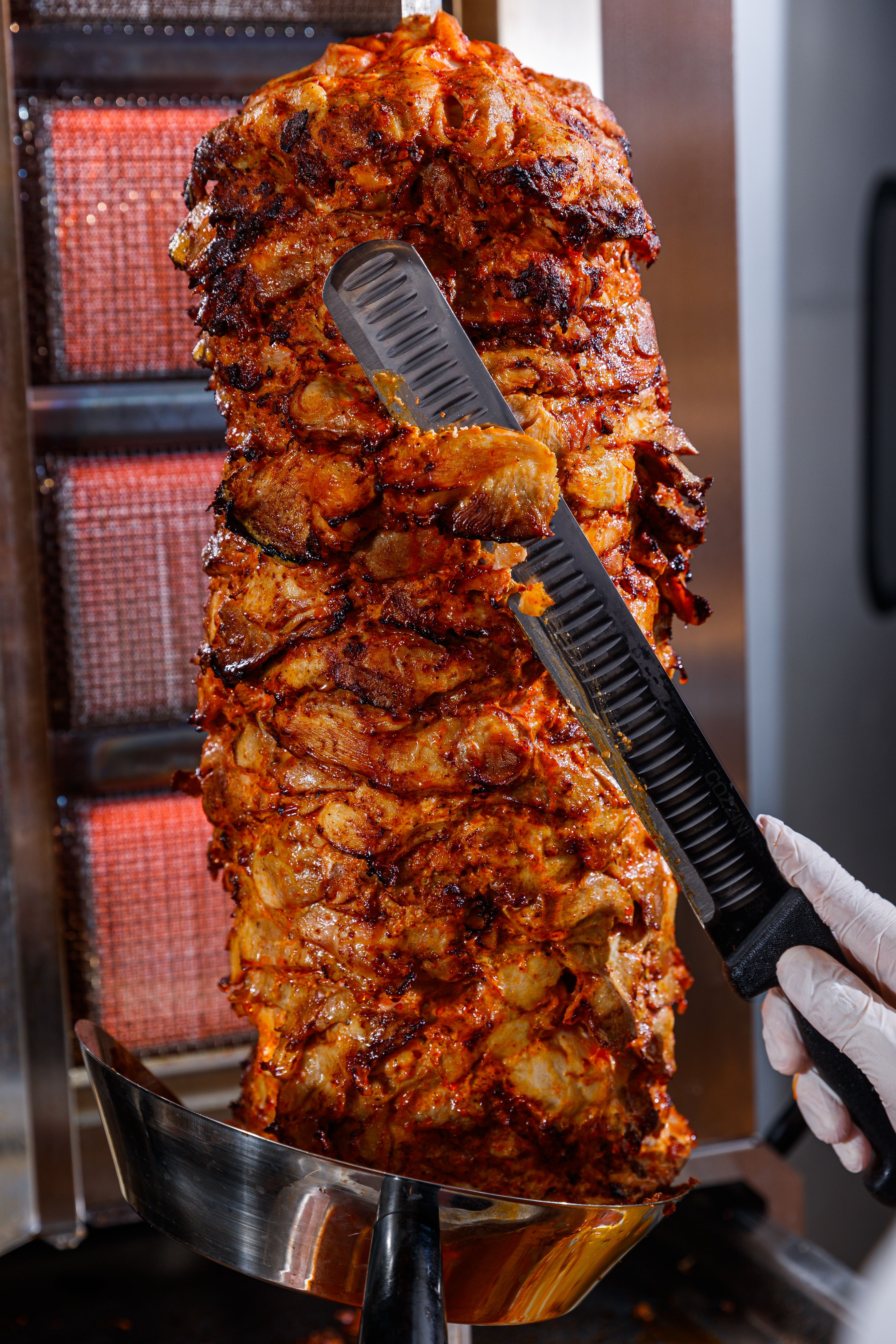 Close-up of shawarma meat being cut from a rotisserie with a knife. Perfect for food photography enthusiasts.
