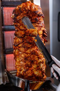 Close-up of shawarma meat being cut from a rotisserie with a knife. Perfect for food photography enthusiasts.
