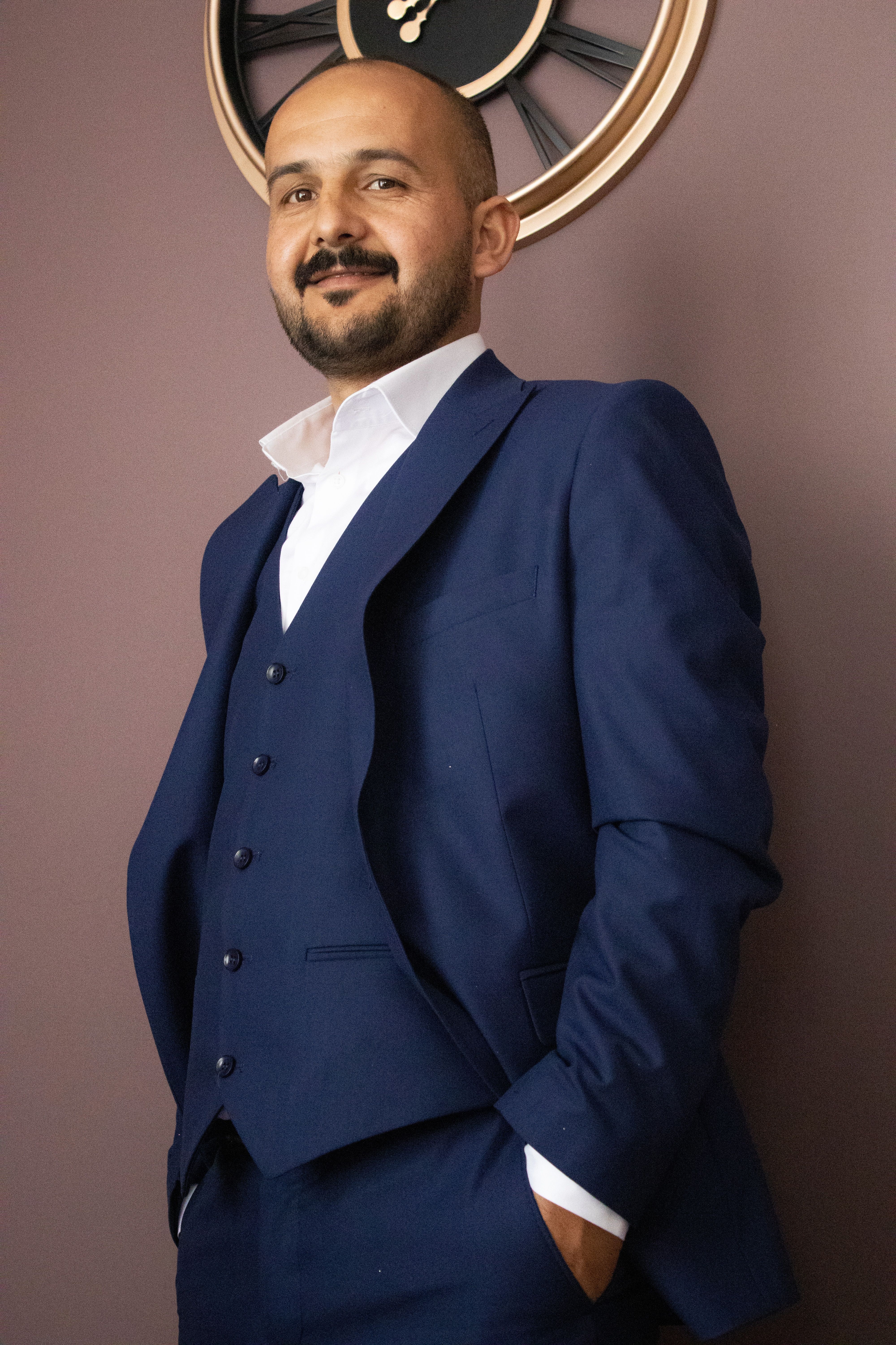 Stylish portrait of a man confidently posing in a blue suit with hands in pockets.