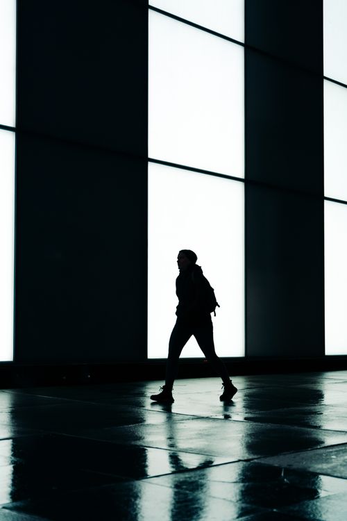 Free Silhouette of a woman walking past illuminated modern architecture in a city environment. Stock Photo