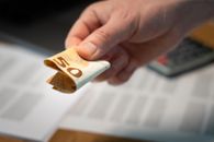 A detailed image of a hand holding a folded 50 euro banknote, with documents in the background.