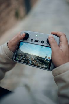 Close-up of hands holding a drone controller with cityscape on screen.