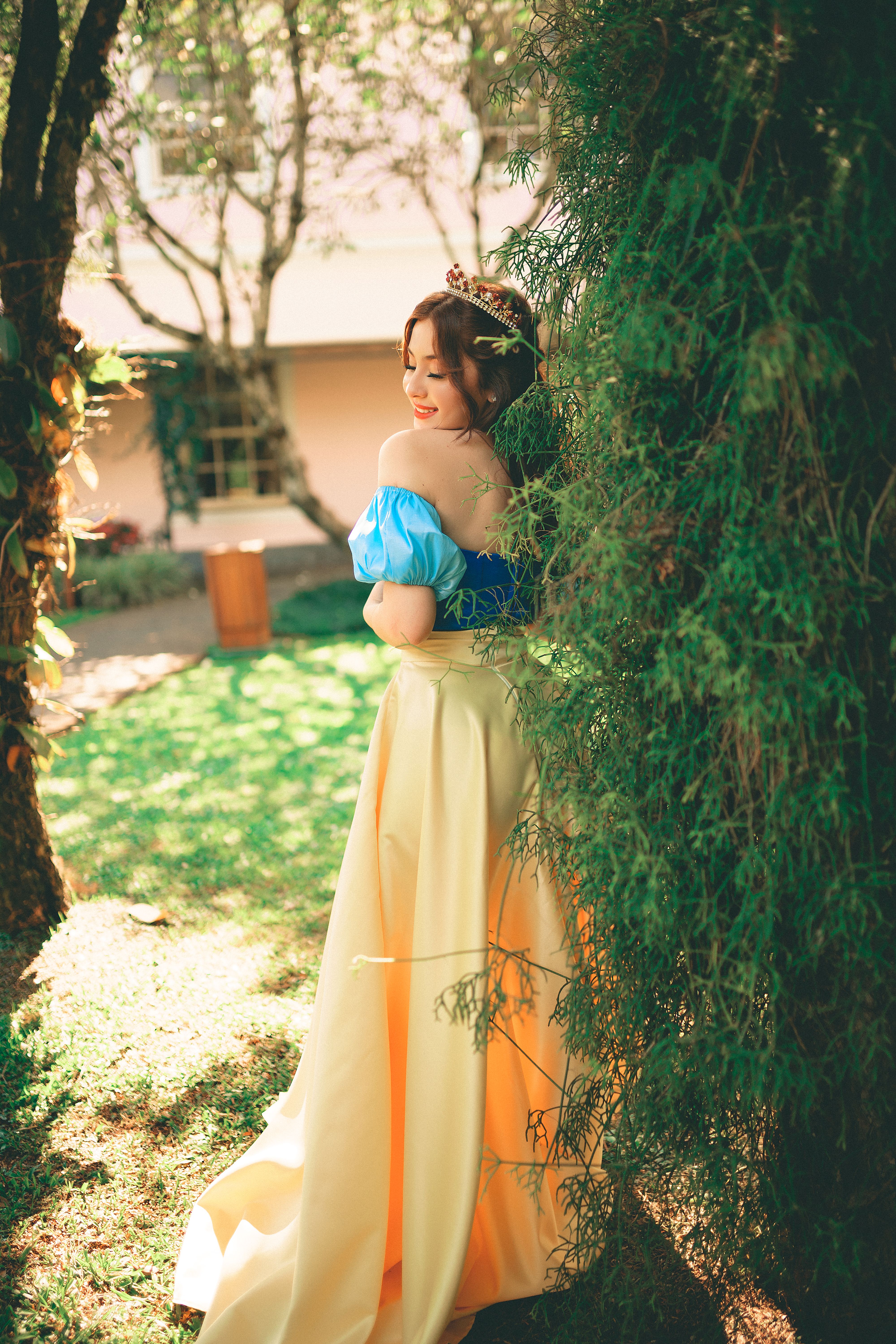 A woman elegantly poses outdoors in a colorful dress and tiara, embodying grace and style.