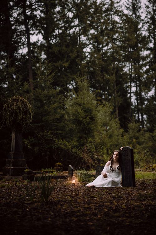 Free Eerie scene of a woman in a white dress sitting by a tombstone in a dark forest. Stock Photo