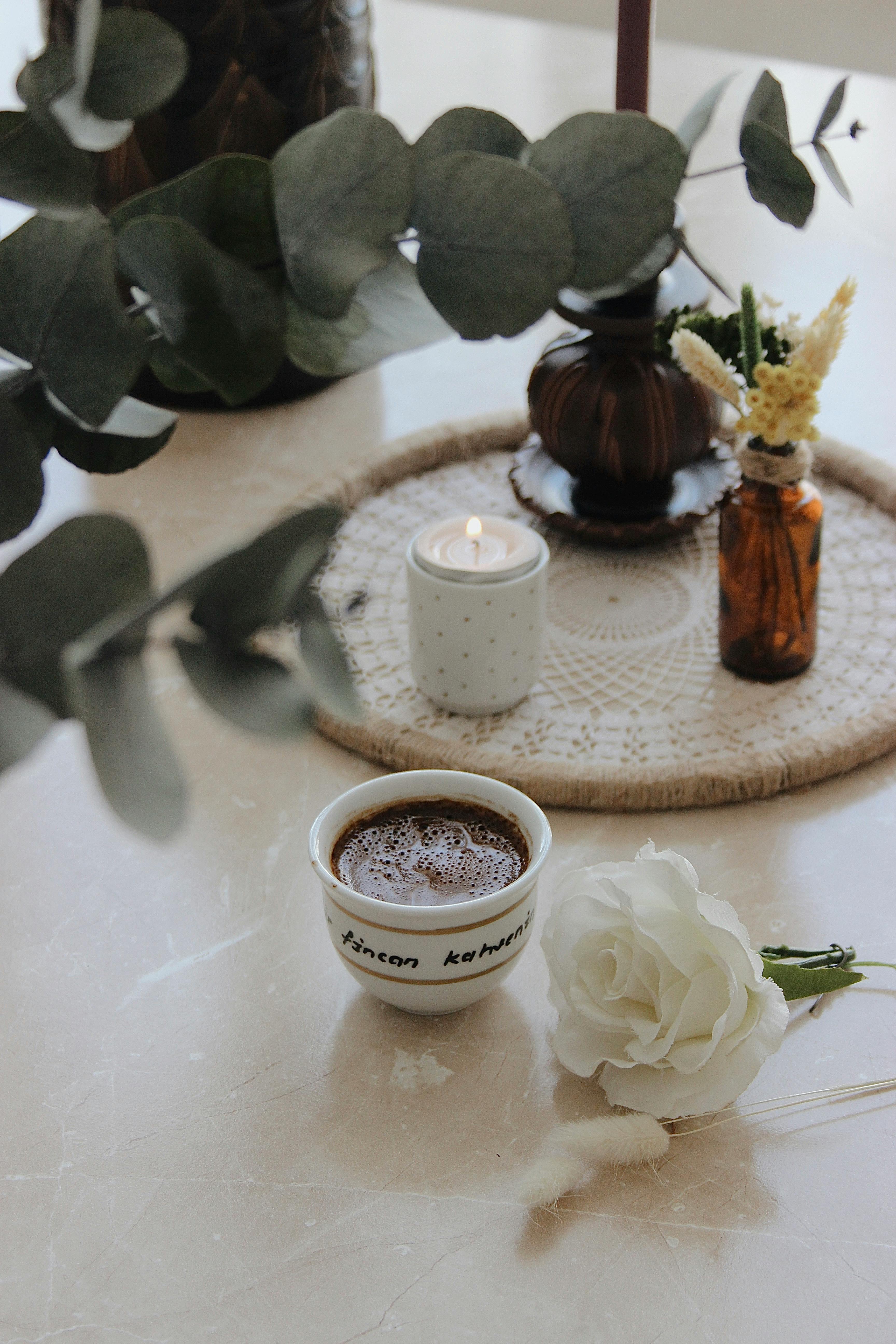 A warm and elegant coffee setup with a candle, flowers, and a cup of coffee on a marble table.