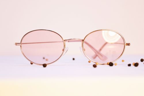 Free Elegant round sunglasses with pink lenses on a minimalist surface, surrounded by peppercorns. Stock Photo