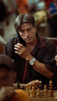 A man with short hair plays chess while talking on the phone at a market in Colombia.