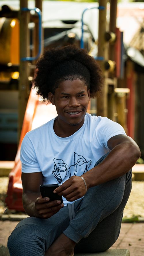 Free Casual portrait of a smiling young man sitting outdoors holding a smartphone. Stock Photo