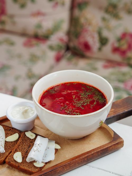 Free Close-up of vibrant red borscht soup served with rye bread and cream on a wooden tray. Stock Photo