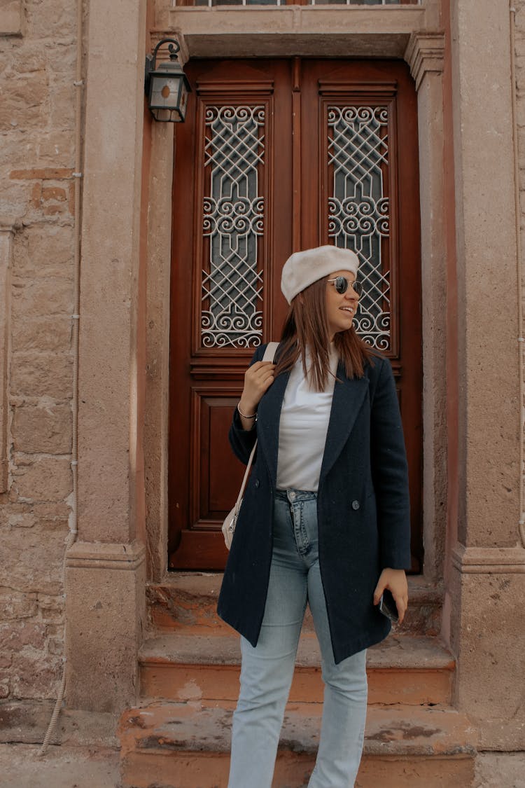 Woman In Blue Jeans And Black Coat Standing With A Phone In Her Hand 