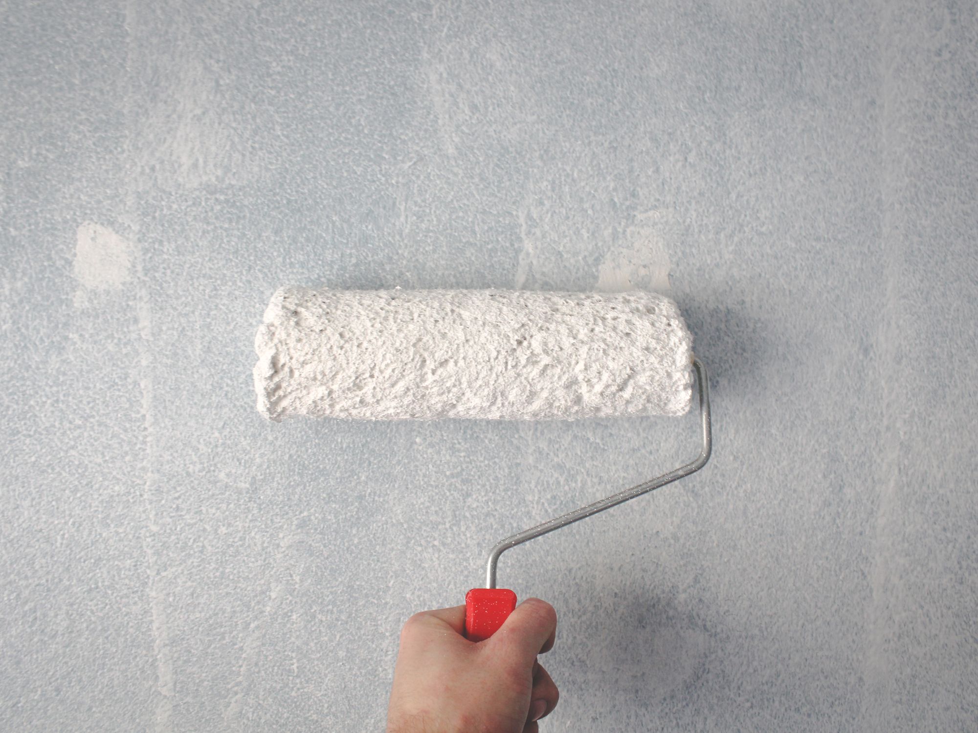 Close-up of a paint roller laying smooth white paint onto a wall