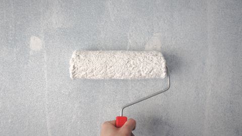 A person's hand using a paint roller to apply white paint on a wall.