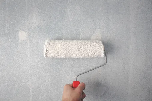 Rodillo de pintura aplicando capa blanca en pared durante reforma de habitación