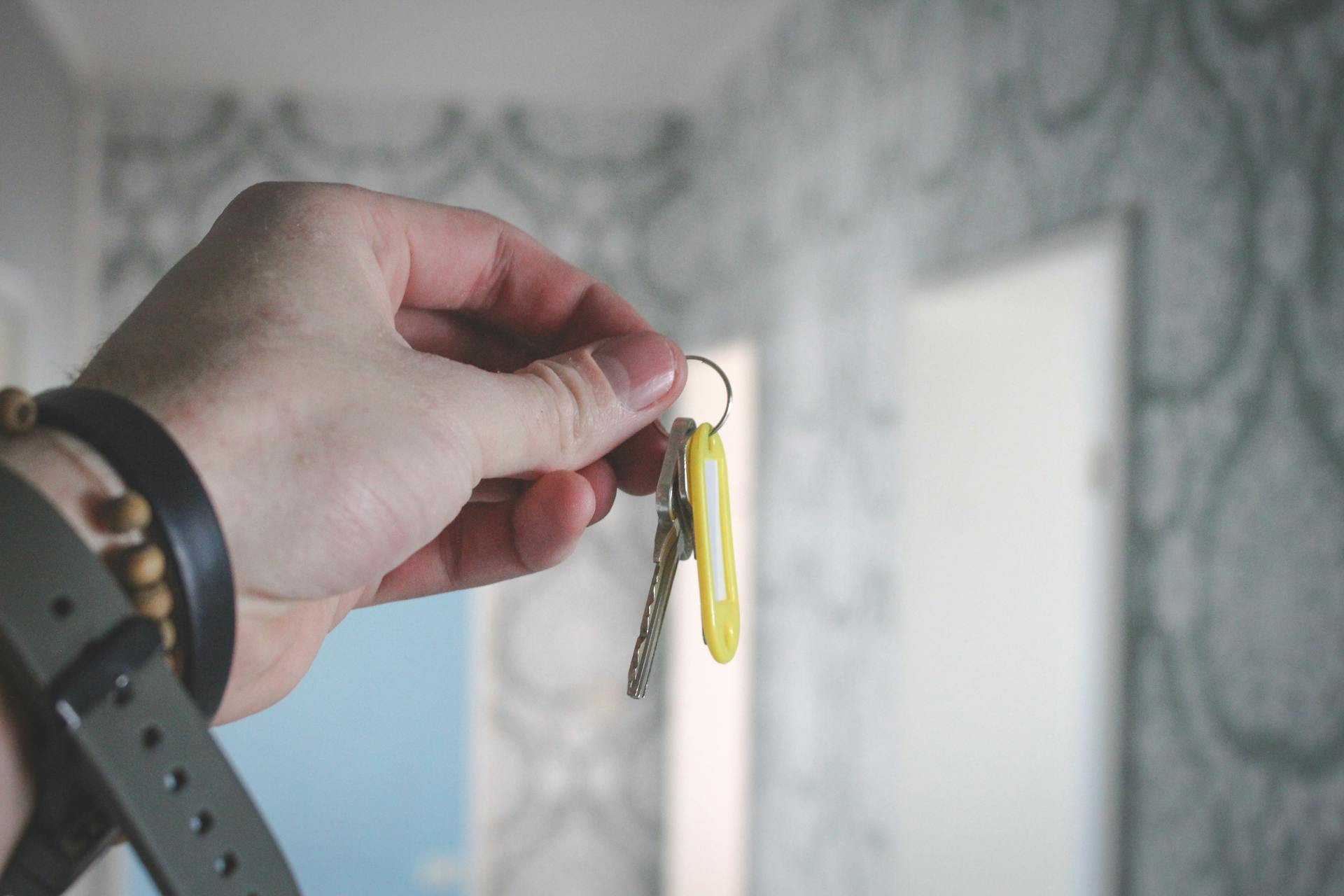 A hand holding a key against a blurred background of patterned wallpaper indoors.