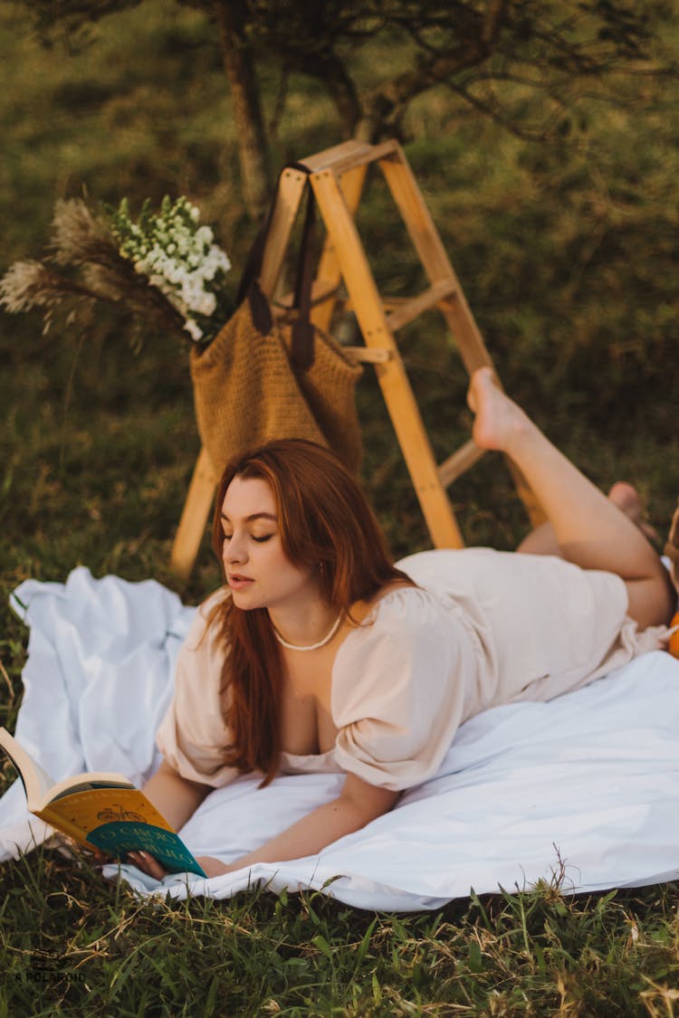 Woman Lying On Grass In Garden Reading Book