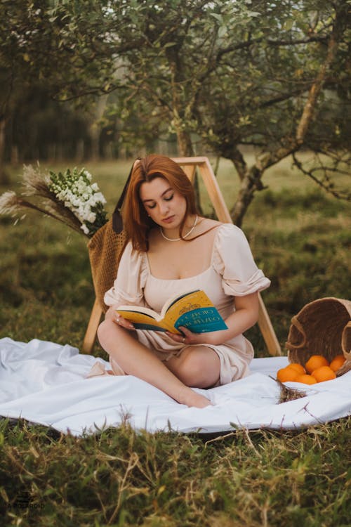 Woman Sitting on Grass in Garden Reading Book