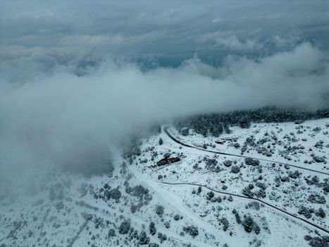 A beautiful aerial shot of a foggy, snow-covered mountain landscape and winding road.