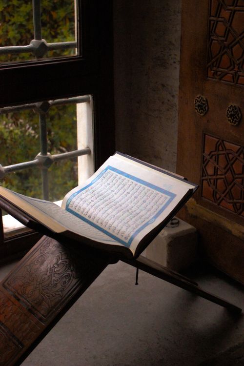 Free A Quran on a wooden stand by a mosque window, showcasing Islamic tradition. Stock Photo