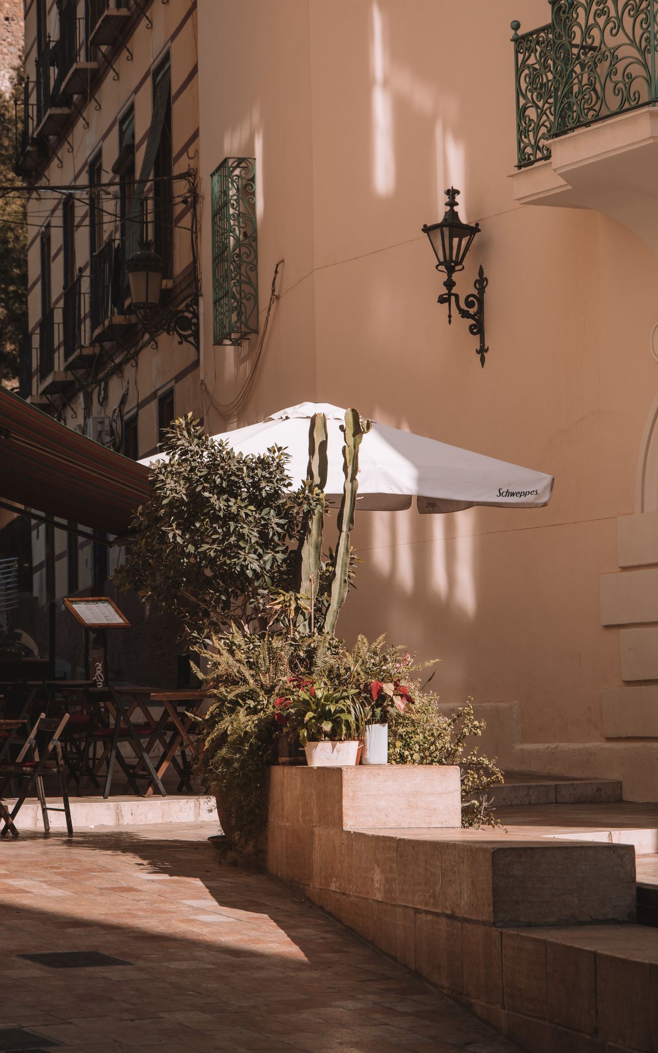 A serene street in Málaga, Spain, showcasing retro architecture, lush greenery, and decorative balcony in warm sunlight.