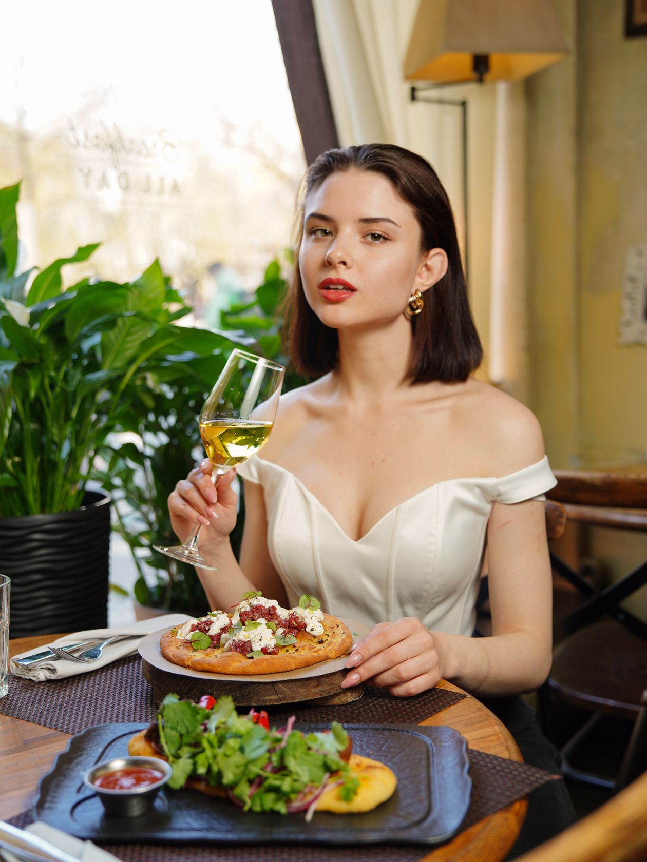 Woman in a white off-shoulder dress holding a wine glass at a restaurant table